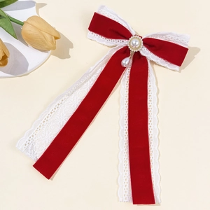 Detailed macro view of a red velvet bow clip with white lace trim and pearl pendant