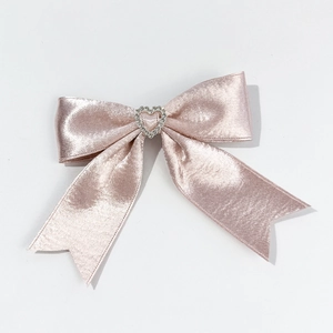 Close-up of pink satin bow hair clip with a sparkling heart-shaped rhinestone center