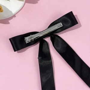 Elegant black satin bow hair clip with crystal accents on a pink background