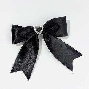 Detail of black satin bow hair clip with a sparkling heart-shaped rhinestone center