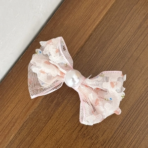Détail d'une pince à cheveux à nœud en dentelle rose avec une grande perle blanche polie