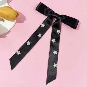 Detail of black satin bow hair clip with sparkling silver star rhinestones on pink background