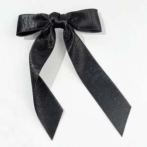 Macro shot of elegant black satin bow hair clip with glossy silk texture and long tails