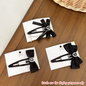 Détail de barrettes à nœuds en satin noir avec strass en cœur sur carte de présentation