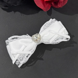 Close-up of a white lace bow hair clip featuring a sparkling heart-shaped crystal detail