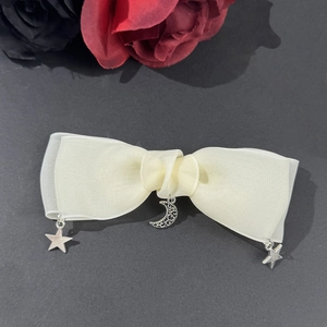 Détail du nœud papillon crème avec pendentifs en argent en forme de lune et d'étoile