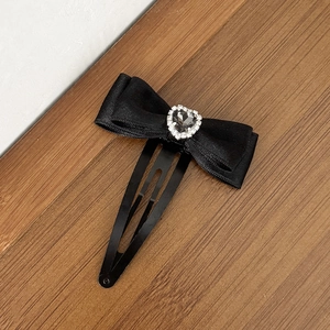 Détail d'une barrette à nœud en soie noire avec un strass en forme de cœur brillant