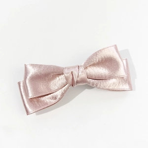 Detailed macro view of the elegant rose gold satin double bow hair clip on white background