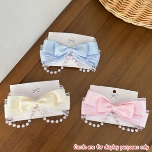 Detailed view of satin bow hair clips with lace trim and hanging pearl chains in pastel tones