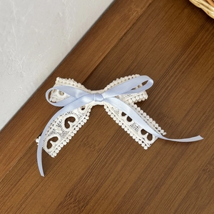 Close-up of cream lace ribbon hair clip with blue satin bow and heart pattern details