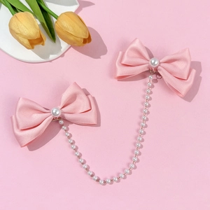 Pink satin bow hair clips with white pearls and hanging chains on a soft pink background