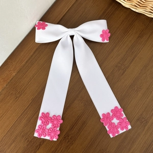 Détail d'un nœud papillon en satin blanc avec fleurs 3D roses sur bois sombre