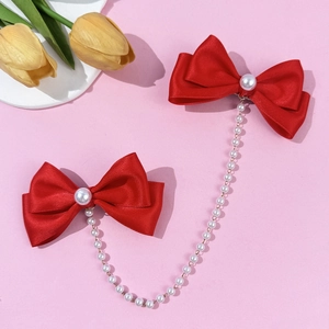 Detail of red satin bow hair clips with white pearl centers and long tassel chain link
