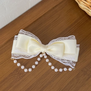 Cream Lolita bow hair clip with lace edges and elegant pearl tassels in a warm scene