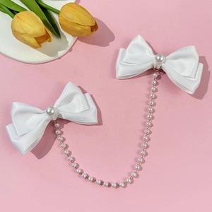 Detail of white satin bow hairpins with long pearl tassels on pink background