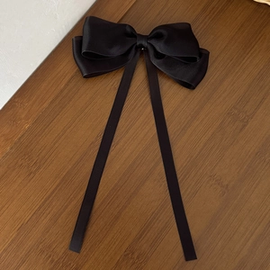 Detailed top view of a black tulle bow hair clip with long ribbons on a wooden desk