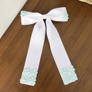 Détail d'un nœud papillon blanc avec broderie florale verte sur une table en bois