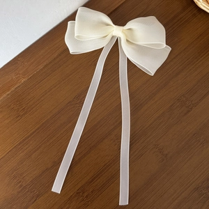 Detail of a creamy white organza bow hair clip with elegant long streamers on wood