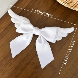 Detailed size view of a white angel wing bow hair clip on a dark wooden background