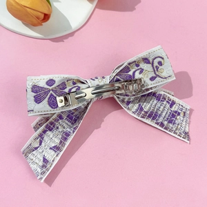 Detail of white embroidered bow hair clip with purple floral patterns and metal spring clip