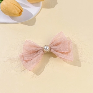Detail of pink chiffon bow hair clip with faux pearl and feathered edges on warm background