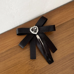 Détail d'une pince à cheveux nœud en satin noir avec un cœur en strass brillant
