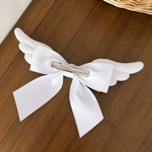 White plush angel wing bow hair clip with satin ribbon on a dark wood background