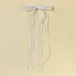 Detail of white organza bow hair clip with long ribbon streamers and wavy edges