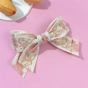 Detail of floral embroidery with pink and gold threads on a white ribbon hair clip