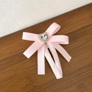 Pince à cheveux nœud rose avec strass en forme de cœur sur fond de bois naturel