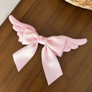 Pink plush angel wing hair clip with a satin bow on a rustic wooden tabletop