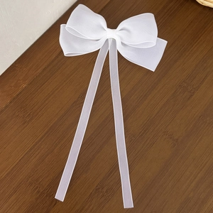 Macro detail of large white sheer mesh bow hair clip with long elegant ribbons on wood