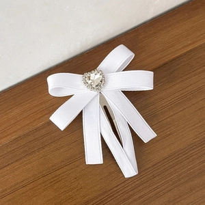 Détail d'une pince à cheveux avec nœud blanc et strass en forme de cœur sur fond de bois