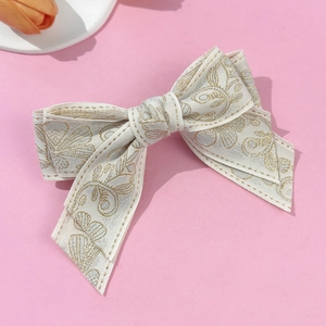 Ethnic style white bow hair clip with gold floral embroidery on a soft pink background