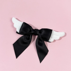 Detail of cute black satin bow hair clip with white plush angel wings on pink surface