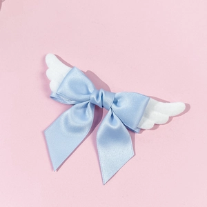 Detail of light blue silk bow with white plush angel wings hair clip on pink background