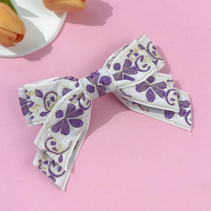 Detail of white bow hair clip with purple floral embroidery and gold edge on pink background