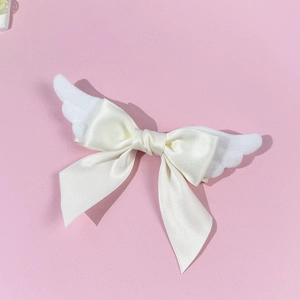Close-up of plush angel wings and satin bow hair clip on a soft pink background