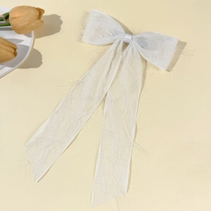 Macro view of white textured chiffon bow hair clip with elegant long ribbons on beige base