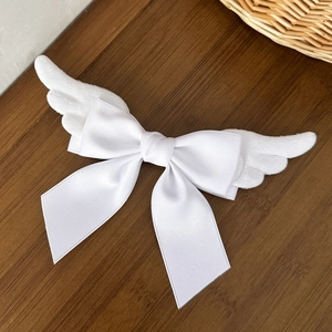 Close-up of white plush angel wings and silk bow hairpin on a dark wooden background