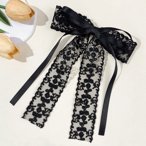 Close-up of black floral lace bow hairpin with elegant long ribbons on creamy background