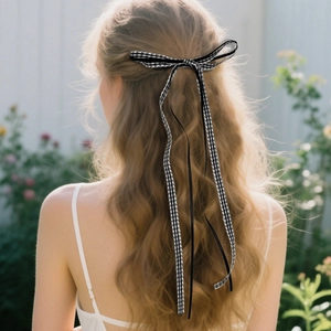 Close-up of gingham bow hair clip with long black ribbons on wavy blonde hair