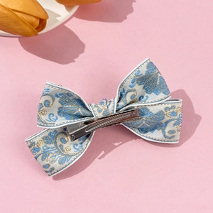 Close-up of floral embroidery on light blue bow hair clip with silver alligator metal grip
