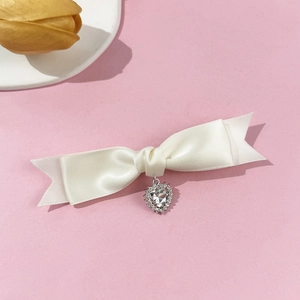 Dettaglio fermaglio a fiocco in raso panna con ciondolo a cuore decorato con strass