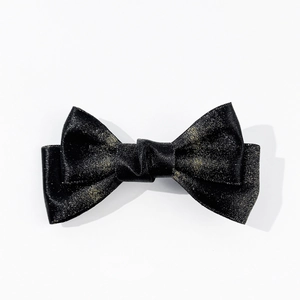 Macro detail of elegant black satin bow hair clip with sophisticated gold glitter finish