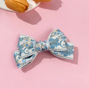 Detail of elegant cream bow hair clip with vintage blue and gold floral embroidery