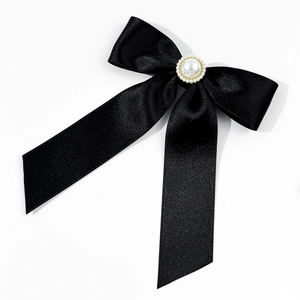 Detailed view of black satin bow brooch with a central pearl and golden metal trim