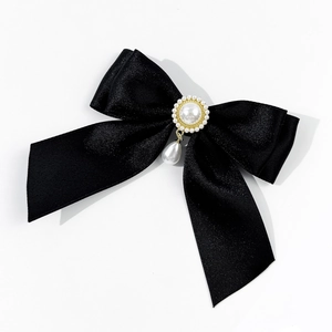 Detail of black satin bow brooch with ornate gold accents and dangling pearl pendant
