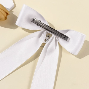 Detail view of white silk ribbon hair bow with heart pendant and silver alligator clip