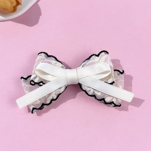 Elegant white lace bow hair clip with black wavy embroidery on a pink background